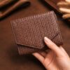 Tannor woven leather envelope wallet in dark chocolate, held in hand to show the compact size